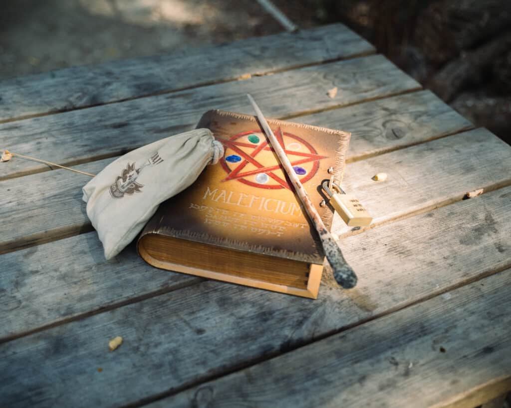 Grimoire Maleficium et Accessoires Magiques sur Bois Grimoire Maleficium, baguette, bourse et cadenas sur table en bois.