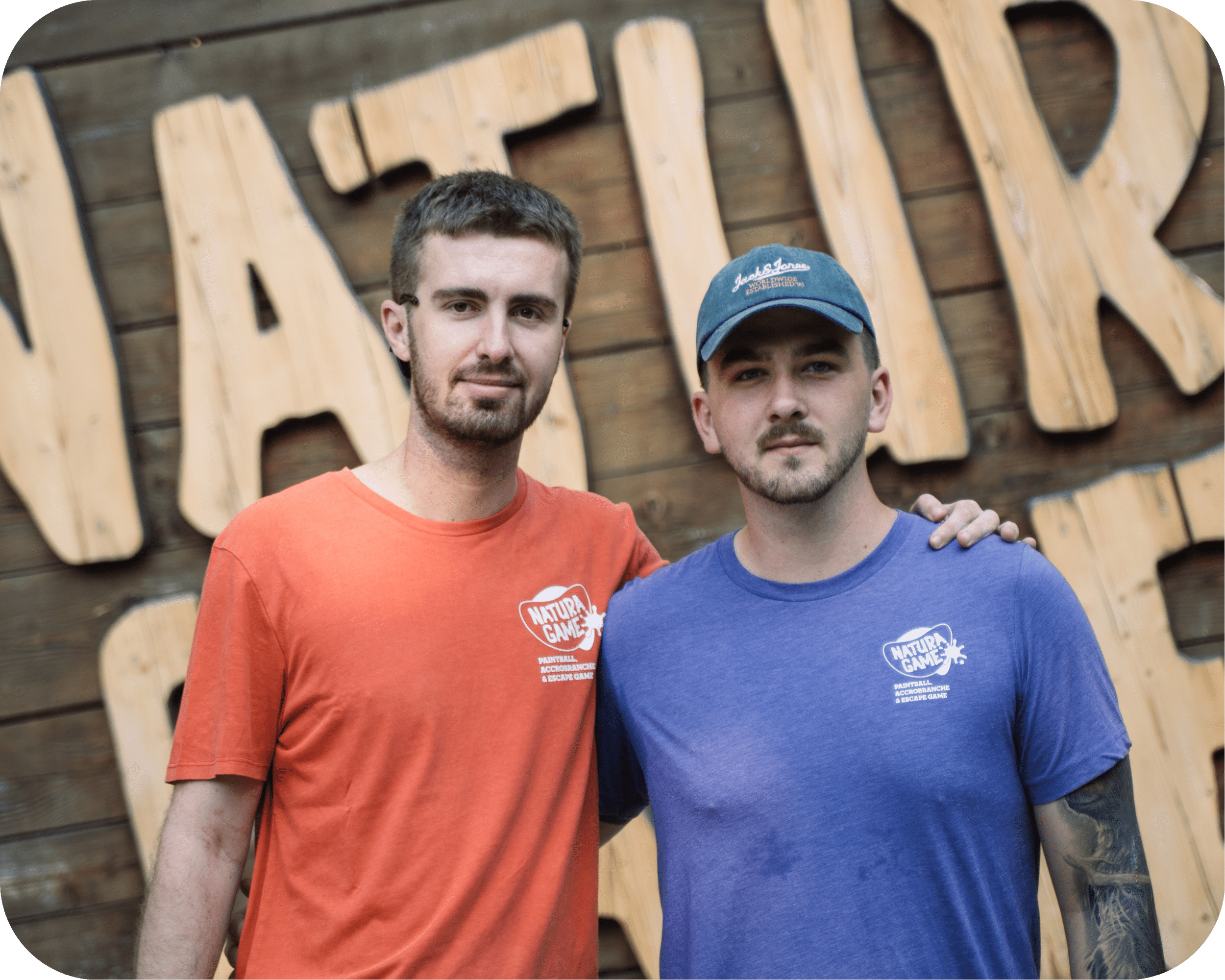 Natura Game : Paintball et Accrobranche entre amis Deux hommes en t-shirts Natura Game posant devant une enseigne en bois, Paintball et Accrobranche.