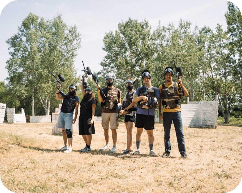 Session Paintball : Groupe Équipé sur Terrain Boisé Six joueurs de paintball posant avec masques et lanceurs sur un terrain extérieur boisé.